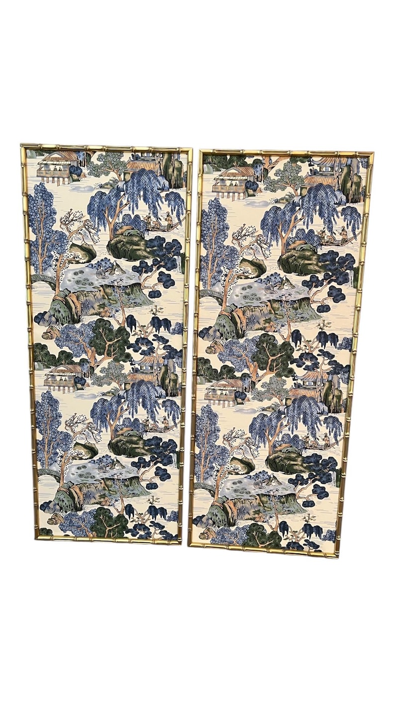 May include: Two rectangular wall panels with a bamboo-style gold frame. The panels feature a scenic landscape design in shades of blue, green, and beige, depicting trees, houses, and water features. The overall aesthetic is reminiscent of traditional Asian art.