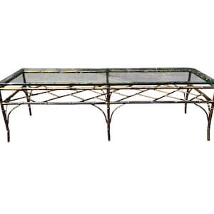 May include: Rectangular coffee table with a clear glass top and a gold-colored bamboo-style metal frame. The table has a geometric design and four legs. The table is suitable for a living room.