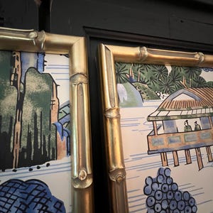 May include: Two framed prints with gold bamboo-style frames. The artwork features a landscape scene with trees, a bridge, and figures. The color palette includes blue, green, and gold.