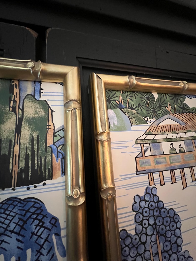 May include: Two framed prints with gold bamboo-style frames. The artwork features a landscape scene with trees, a bridge, and figures. The color palette includes blue, green, and gold.
