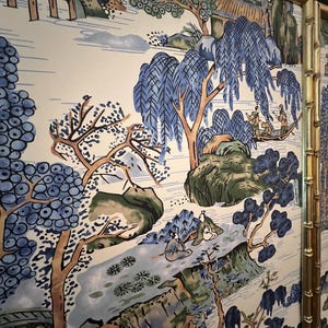May include: A decorative screen featuring a scenic landscape design with blue and green trees, mountains, and figures in boats. The screen has a gold bamboo-style frame, adding a touch of elegance to the artwork.