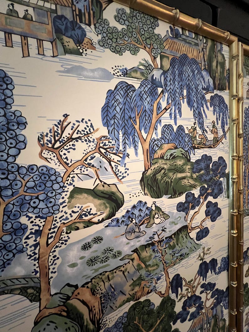 May include: A decorative screen featuring a scenic landscape design with blue and green trees, mountains, and figures in boats. The screen has a gold bamboo-style frame, adding a touch of elegance to the artwork.
