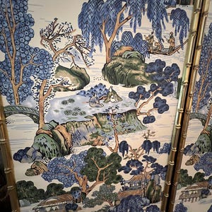 May include: A decorative panel featuring a serene Asian landscape scene. The artwork showcases a river, bridges, and traditional buildings, all rendered in shades of blue, green, and beige. The panel is framed with gold bamboo-style accents.