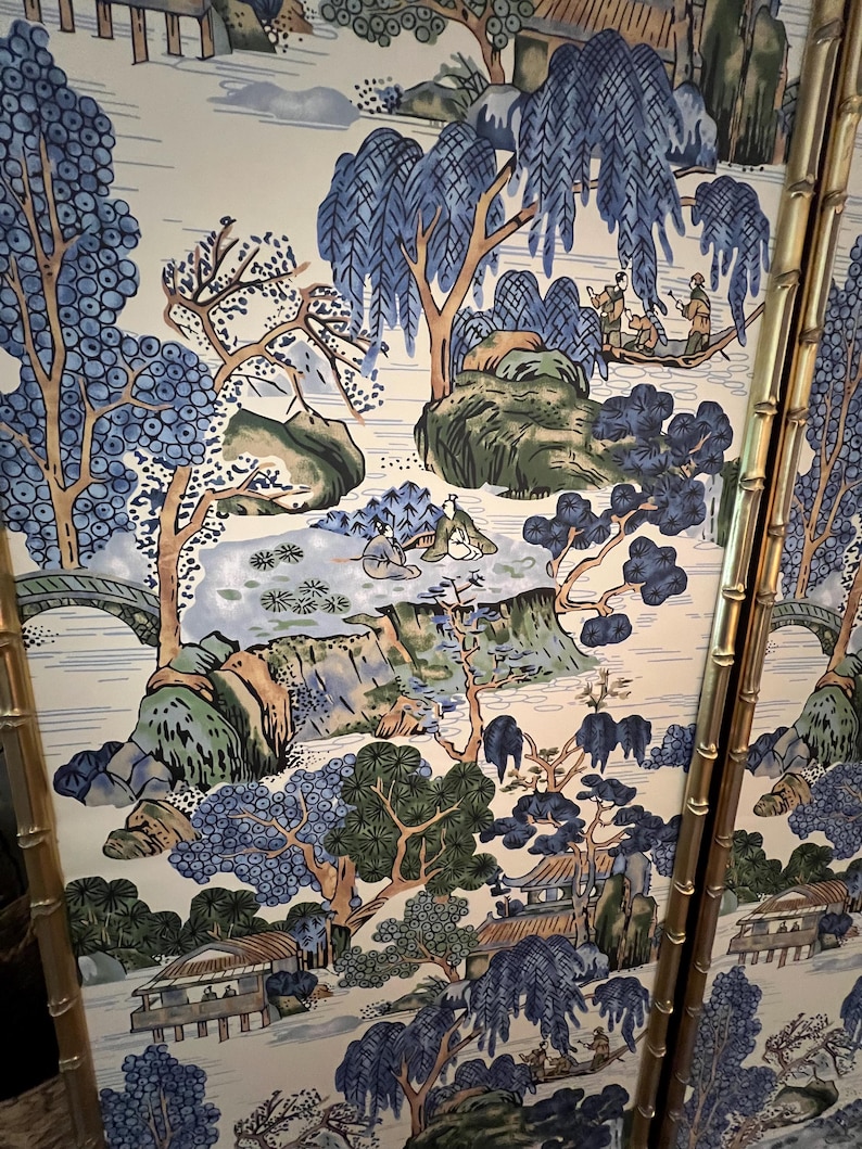 May include: A decorative panel featuring a serene Asian landscape scene. The artwork showcases a river, bridges, and traditional buildings, all rendered in shades of blue, green, and beige. The panel is framed with gold bamboo-style accents.