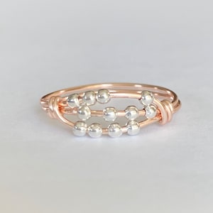 May include: A rose gold ring with three rows of silver beads. The beads are evenly spaced and the ring is made of wire.