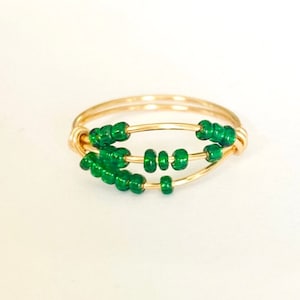 May include: A gold ring with three rows of green beads. The ring is made of thin wire and the beads are small and round.