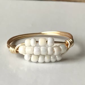 May include: A gold wire ring with white beads woven into the wire. The ring is simple and delicate.