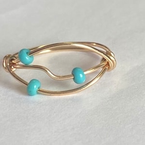 May include: A gold ring with a wavy design and three turquoise beads.