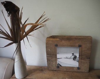 May include: A rustic wooden picture frame with a black and white photo of a person in a boat. The frame is made of reclaimed wood and has a clear acrylic front.