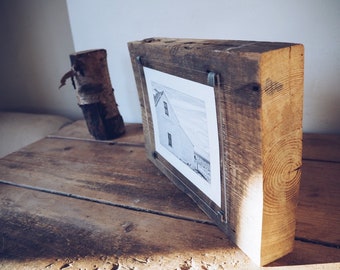 May include: A rustic wooden picture frame with a black and white photograph of a house. The frame is made of reclaimed wood and has a natural finish. The photo is held in place by clear acrylic.