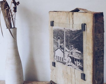 May include: A rustic wooden picture frame with a black and white photo of a building with a tall chimney. The frame has a rusty metal strip along the bottom and the words "SUPPORT EVER" are printed on the side.