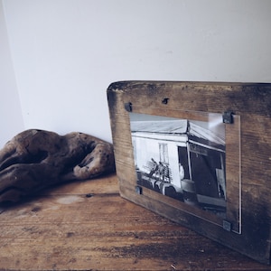 May include: A rustic wooden picture frame with a black and white photo of a building. The frame has a distressed finish and is held together with metal brackets.