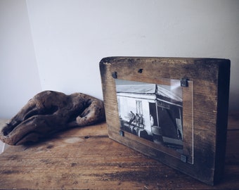 May include: A rustic wooden picture frame with a black and white photo of a building. The frame has a distressed finish and is held together with metal brackets.