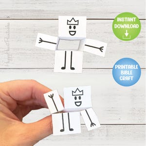 May include: A white paper craft shaped like a person with a crown, arms, and legs. The face has a simple design with a smile and the letter "D". The image includes the text "Instant Download" and "Printable Bible Craft".