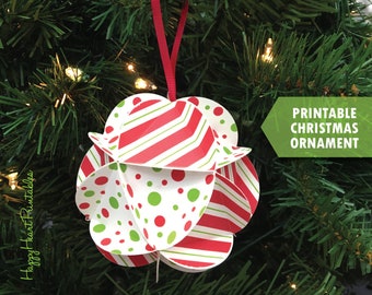 Puede incluir: Adorno navideño de papel con rayas rojas y blancas y lunares verdes. El adorno cuelga de una cinta roja sobre un fondo de un árbol de Navidad verde. El texto en la imagen dice "Printable Christmas Ornament".