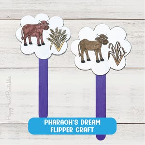 May include: Two flipper crafts featuring purple popsicle sticks attached to cloud-shaped paper cutouts. Each cutout displays a hand-drawn illustration of a brown cow and a stalk of wheat. The text "PHARAOH'S DREAM FLIPPER CRAFT" appears in blue.