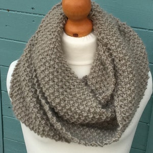 May include: A light brown knitted infinity scarf. The scarf is made from a soft, textured yarn and is ideal for keeping warm in the winter.