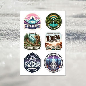 Op de afbeelding: Zes kleurrijke ronde stickers met verschillende fantasielandschappen en tekst. De stickers tonen een bergketen met een kasteel, een waterval in een bos, een beer in een bos, een meer met ijsformaties, een bergketen met een vogel en een bos met een hoge boom.