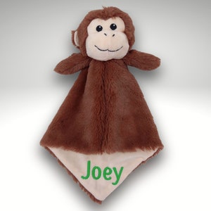 May include: Brown plush monkey security blanket with a beige underside. The blanket has the name "Joey" embroidered in green on the beige side.