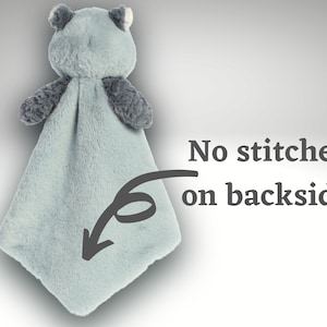 May include: A plush security blanket featuring a light blue, soft-textured fabric body with a stuffed animal head and dark gray arms. The text "No stitches on backside!" is printed next to an arrow pointing to the smooth, seamless fabric.