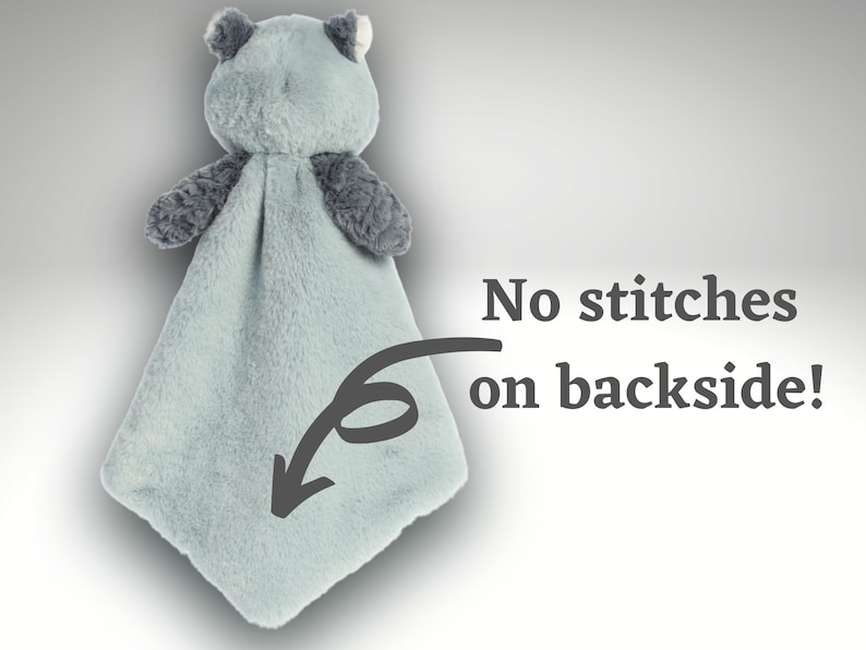 May include: A plush security blanket featuring a light blue, soft-textured fabric body with a stuffed animal head and dark gray arms. The text "No stitches on backside!" is printed next to an arrow pointing to the smooth, seamless fabric.