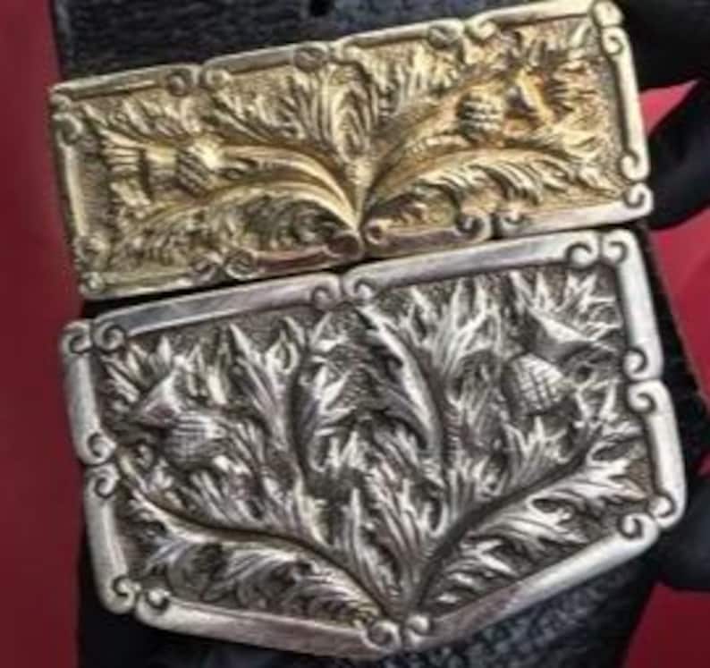 Op de afbeelding: Twee riemgespen met een distelmotief. De bovenste gesp is goud en de onderste gesp is zilver.