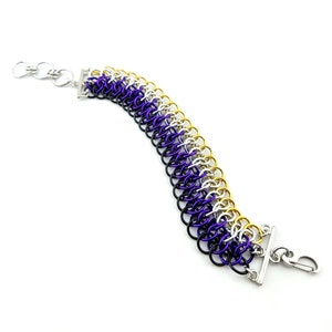 May include: A purple, white, and yellow chainmail bracelet with silver clasps. The bracelet is made of small metal rings.