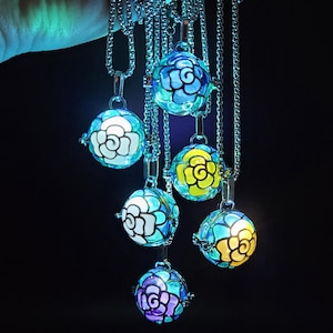 May include: A collection of silver necklaces, each featuring a round, glowing pendant with a floral design. The pendants display a variety of colors, including blue, yellow, and purple, against a dark background.