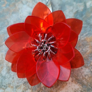 May include: A red plastic flower with a silver metal center. The flower has many petals and is a decorative piece.