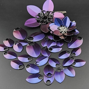 May include: A set of iridescent purple and blue metal scales with a black metal ring on each scale. The scales are arranged in a fan shape. There are two larger scales in the shape of flowers with black metal centers.