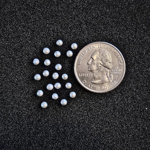 May include: A close-up of a US quarter dollar coin next to a scattering of small, white, pearl-like beads on a black surface.