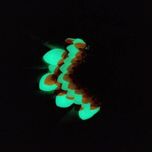 May include: A green and orange glow-in-the-dark dragon scale bracelet. The scales are arranged in a curved pattern.