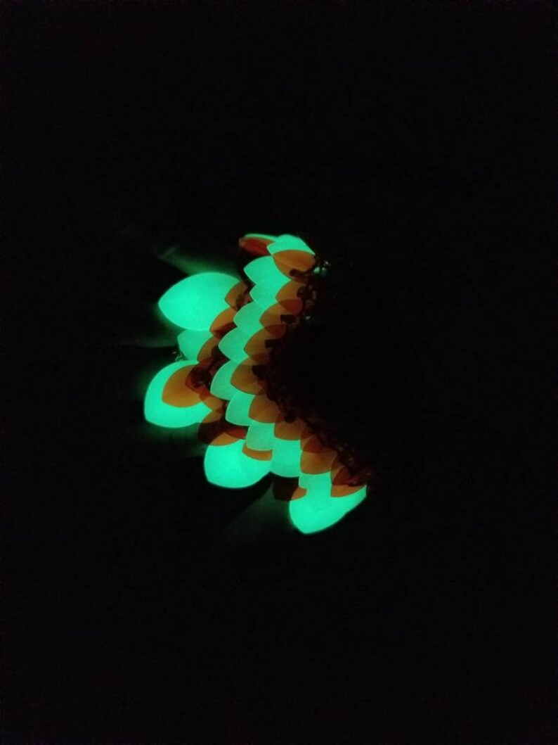 May include: A green and orange glow-in-the-dark dragon scale bracelet. The scales are arranged in a curved pattern.
