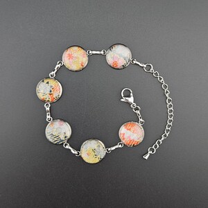 May include: A silver chain bracelet with five round glass charms. Each charm features a different colorful Japanese fabric pattern.