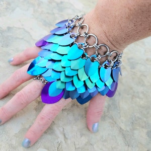 May include: A blue and purple iridescent metal bracelet with a chain link design. The bracelet is made of small, overlapping scales that create a textured look.