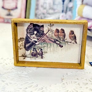 May include: A rectangular wooden frame containing a print of a black and white kitten playing a violin while perched on a fence near several small brown birds. The frame is a natural wood color with a simple, clean edge design surrounding the image.
