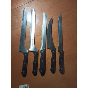 May include: A collection of six stainless steel kitchen knives with black handles. The blades have various shapes, including serrated and curved designs. The knives are displayed on a wooden surface, highlighting their different blade styles.