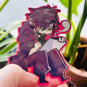 Może przedstawiać: Naklejka z postacią z kreskówki o fioletowych włosach, ubraną w czarny płaszcz i spodnie, siedzącą i rysującą w notesie. Postać ma fioletowe i białe oko i trzyma czerwony długopis.