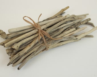 Può includere: Un fascio di bastoncini di legno di deriva naturale legati insieme con uno spago. I bastoncini sono di varie dimensioni e forme, con un colore marrone chiaro.