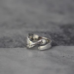 Peut inclure: Une bague en argent avec un motif d'oiseau. La tête de l'oiseau est tournée vers le spectateur et la bague est ouverte sur le côté.