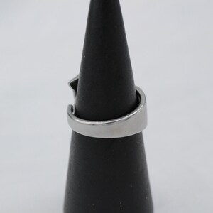 May include: A silver ring with a unique design. The ring is on a black ring display stand.