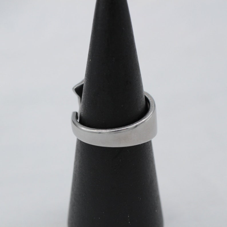 May include: A silver ring with a unique design. The ring is on a black ring display stand.