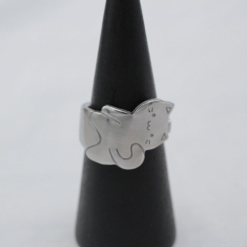 May include: A silver ring with a cat design. The cat is curled up and has a cute face.