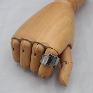 May include: A silver ring with a cat design. The ring is on a wooden hand model.