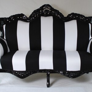 May include: A black and white striped sofa with a black, ornate wooden frame. The sofa has a curved back and arms.