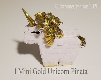 May include: A small white unicorn pinata with gold glitter and a gold horn. The pinata is decorated with gold streamers.
