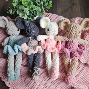 May include: Four handmade crochet mouse dolls in ballet outfits. Each mouse has large ears and is wearing a tutu and ballet slippers. The dolls are in shades of gray, white, and tan, with blue and pink accents. They are arranged on a pink crocheted blanket.