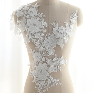 Könnte beinhalten: Weiße florale Spitzenapplikation mit zarten Blüten und Blättern. Diese Spitzenborte ist perfekt, um Brautkleidern, Braut-Accessoires oder anderen Bastelprojekten einen Hauch von Eleganz zu verleihen.