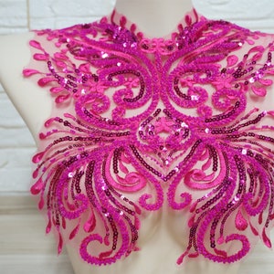 Może przedstawiać: Różowa aplikacja wyszywana i ozdobiona cekinami z kwiatowym wzorem. Aplikacja idealnie nadaje się do dodania blasku i elegancji każdemu ubraniu.