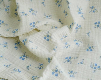 Op de afbeelding: Witte stof met een klein blauw bloemenpatroon. De stof is zacht en heeft een licht getextureerd oppervlak.